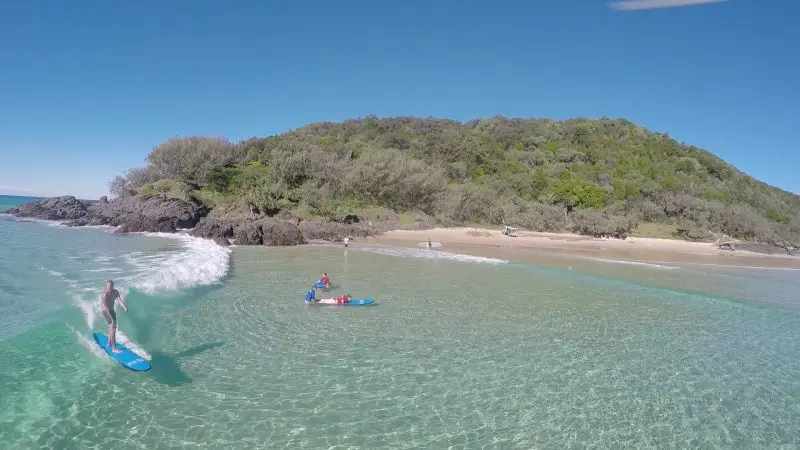 Surfer riding Australia’s longest wave by a scenic island, with another paddler navigating crystal-clear waters nearby.