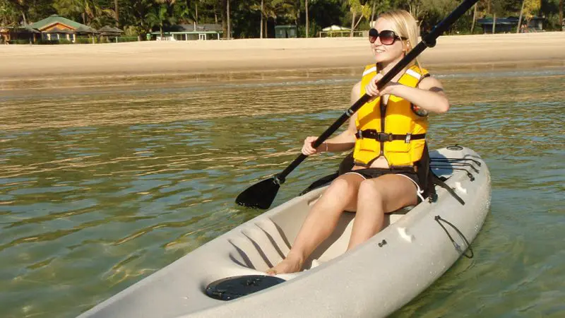 Smiling woman in yellow life jacket and sunglasses kayaking on serene waters during Adventure Moreton Island Day Pass experience.