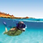 Snorkeller explores vibrant blue waters by a rusted shipwreck on Moreton Island, showcasing Adventure Day Pass for unforgettable experience.