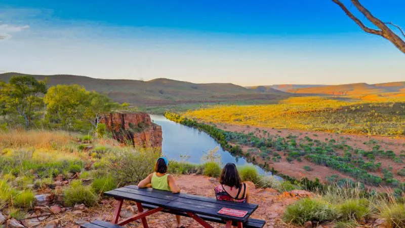 Two travellers enjoy a riverside picnic table view during a 10-day Broome to Darwin Kimberley tour adventure, scenic and relaxing.