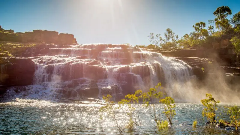 Sunlight illuminates a majestic cascading waterfall, a top attraction on the 10 Day Broome to Darwin Kimberley Off-road Adventure Tour.