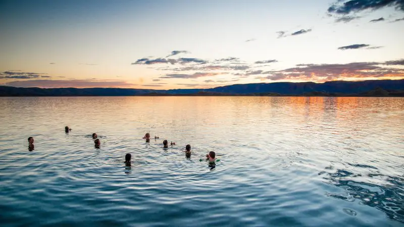 Travellers swimming in a serene lake at sunset, framed by majestic Kimberley mountains on a Broome to Darwin Tour adventure.
