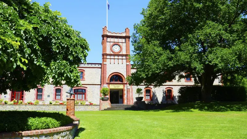 Stunning historic brick building with iconic clock tower, top Barossa Valley Hop On Hop Off Tour stop surrounded by lush lawns and trees.