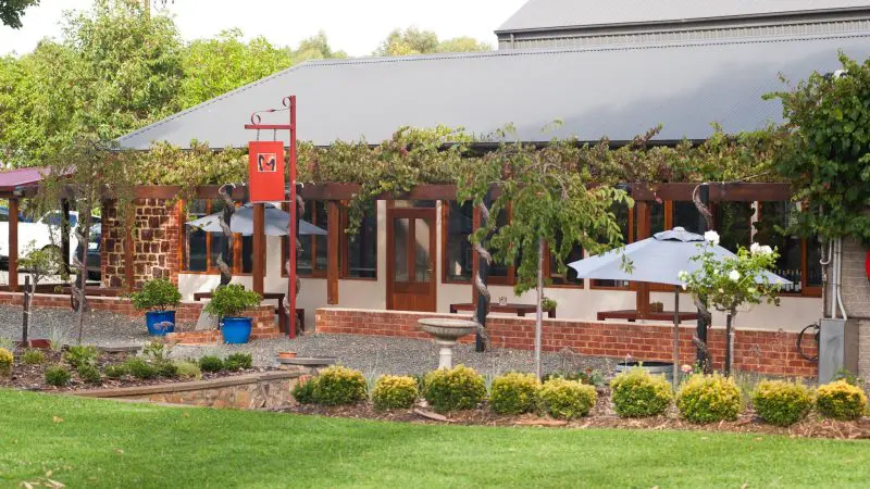 Charming rustic building with lush vine-covered pergola, inviting outdoor seating, and manicured lawn—top Barossa Valley Hop On Hop Off stop.