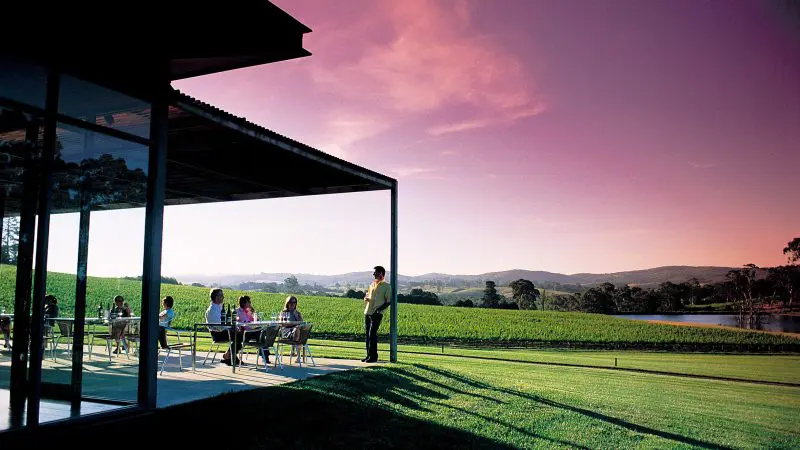 Guests enjoying al fresco dining at a scenic vineyard at sunset on the Hahndorf Adelaide Hills Hop On Hop Off Tour, South Australia.