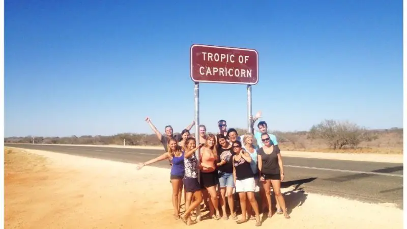 A happy group poses beneath the Tropic of Capricorn sign on their 8-Day Perth to Exmouth Return Tour, enjoying sunny, dry weather.
