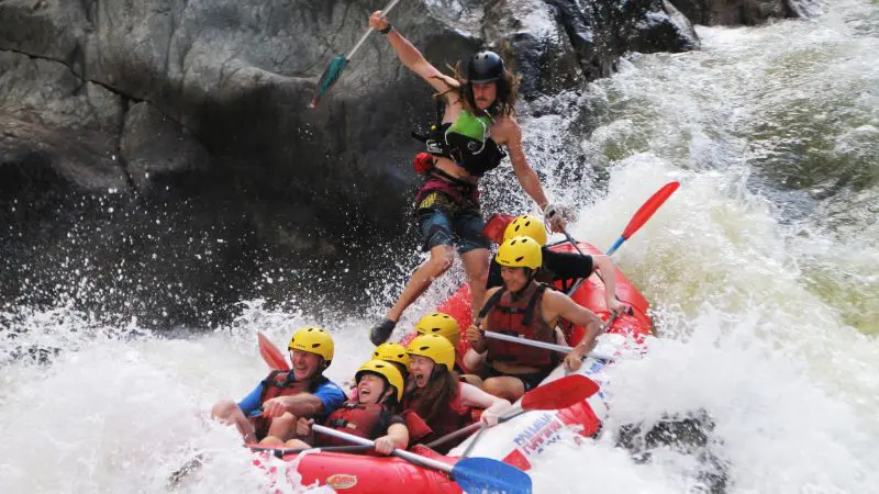 Thrill-seekers in safety helmets navigate intense white-water rapids in a red raft on Barron River Rafting near Port Douglas.