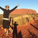 Excited woman jumps on vibrant red dirt track by Uluru, Australia, during a 3-night Rock The Centre Yulara to Yulara tour.