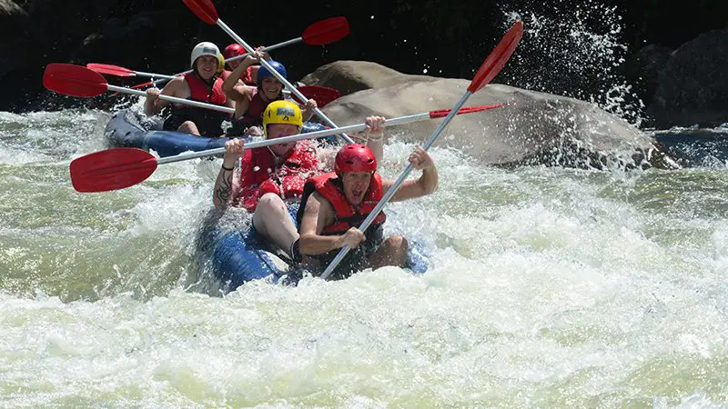 Adventure seekers in helmets and life jackets white-water rafting through thrilling rapids on a full-day Mission Beach excursion.