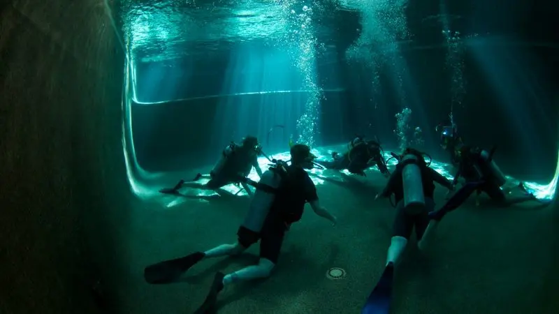 Six scuba divers train underwater in a sunlit pool during an intensive 2 Day PADI Refresher Course, mastering essential diving skills.