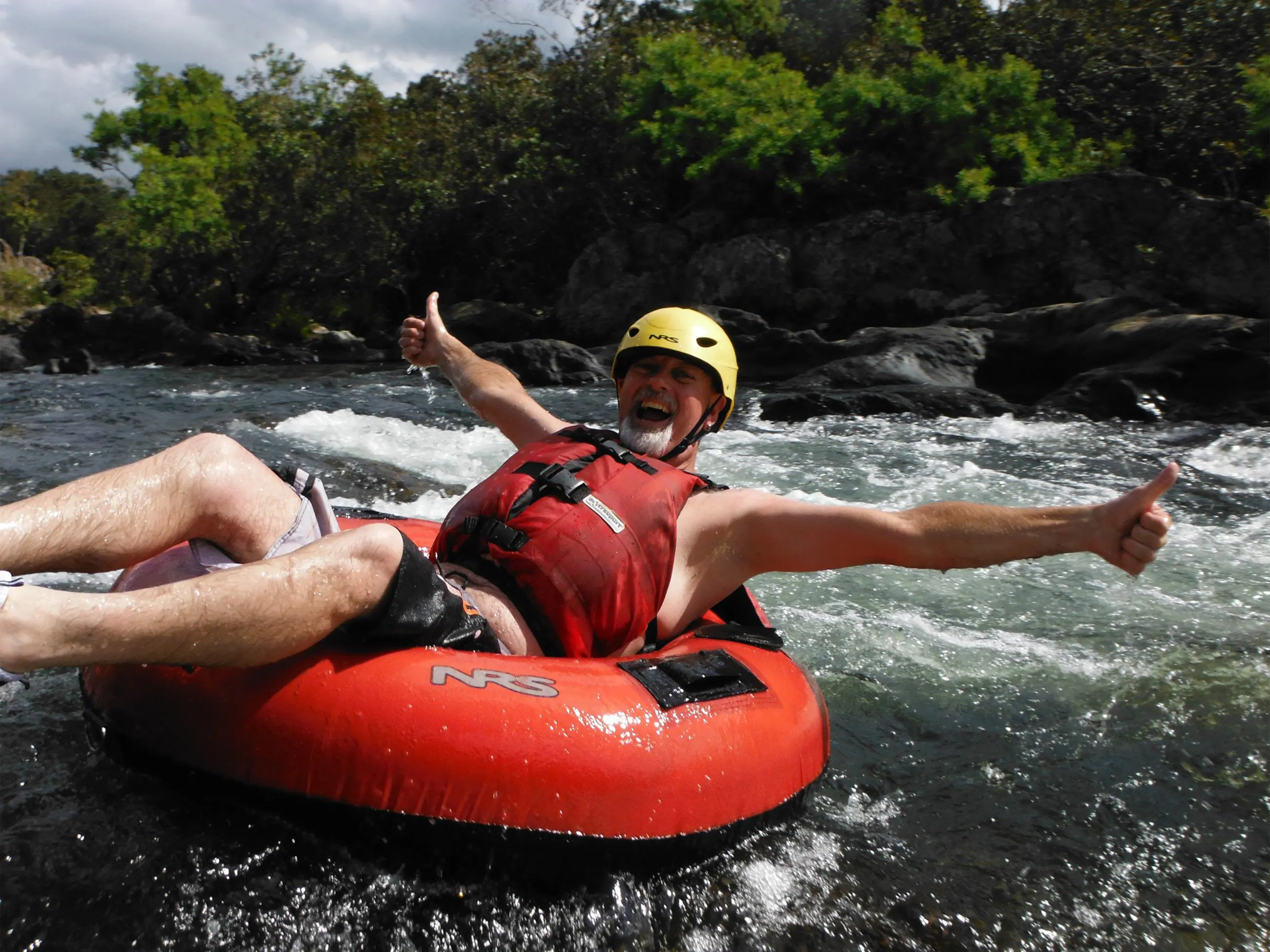 Smiling man wearing a yellow helmet and red vest gives thumbs up during Foaming Fury half-day river tubing adventure experience.