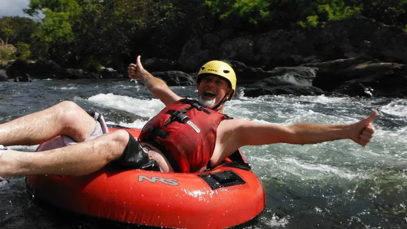 Smiling man wearing a yellow helmet and red vest gives thumbs up during Foaming Fury half-day river tubing adventure experience.