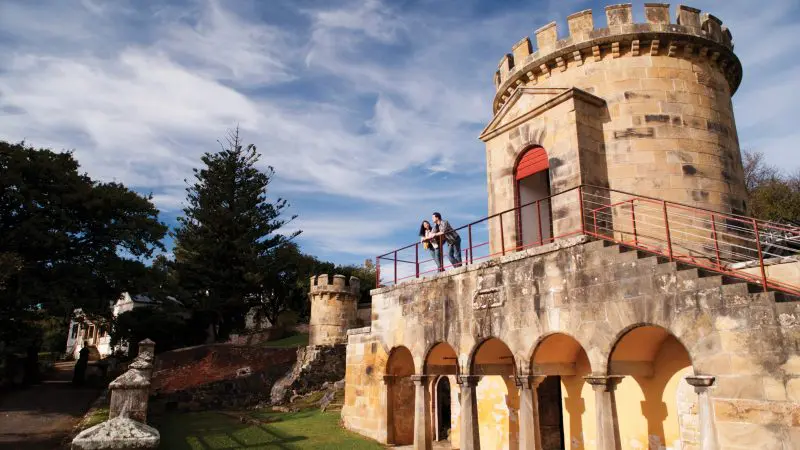 Two visitors on a historic stone fort balcony, enjoying scenic views during the 7 Day Super 7 Tasmania Tour by Under Down Under Tours.