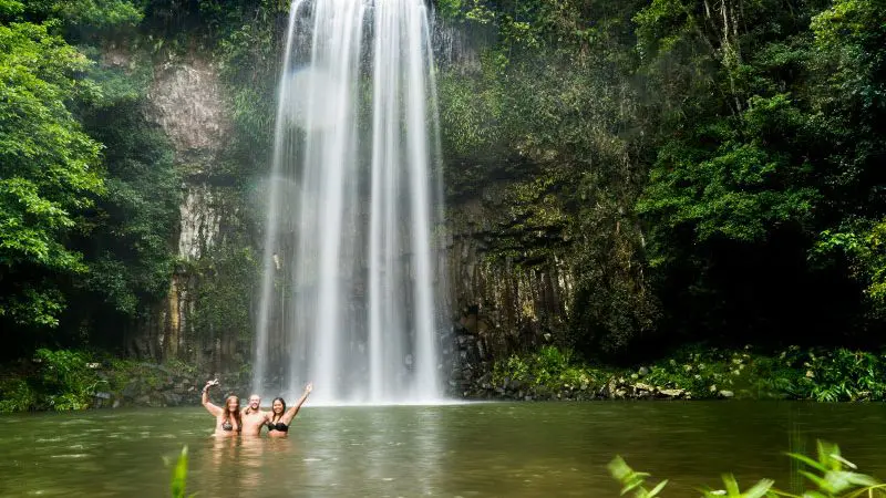 Three travellers raise arms in a vibrant green pool, enjoying a Fully Guided Ultimate East Coast Melbourne to Cairns adventure tour.