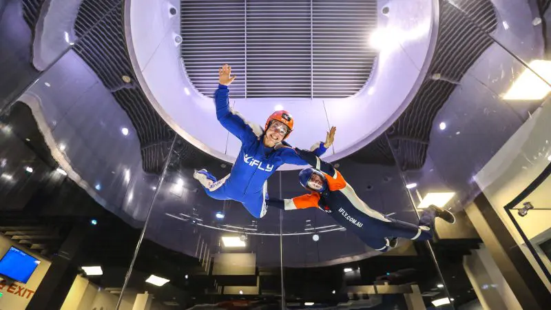 Two people experience indoor skydiving at iFLY Family and Friends, smiling in flight suits and helmets inside a state-of-the-art wind tunnel.