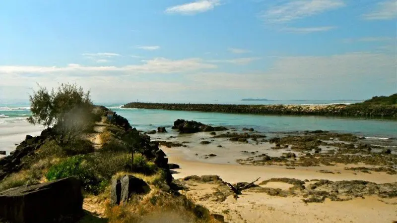 Scenic rocky path to a jetty on Brunswick River Nature Tour, framed by crystal-clear turquoise water and pristine sandy beach.