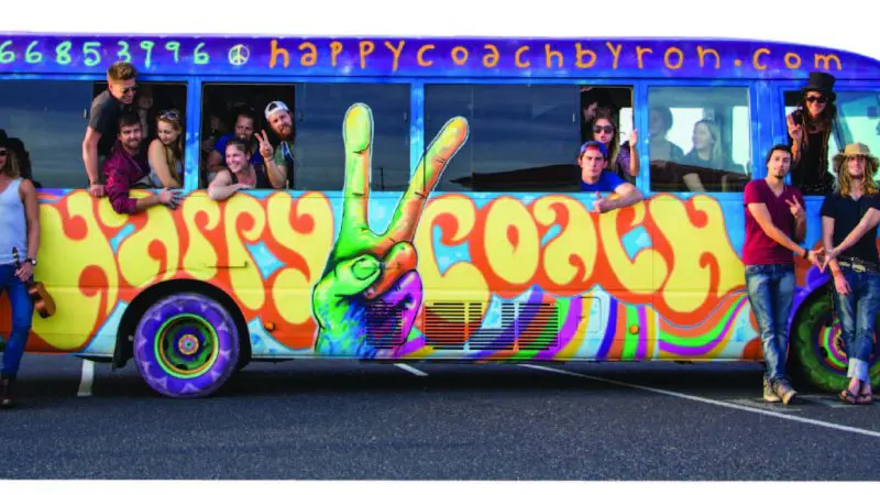 Travellers smile in front of the vibrant Happy Coach bus on a 1 Day Nimbin Tour from Byron Bay, perfect for adventure seekers.
