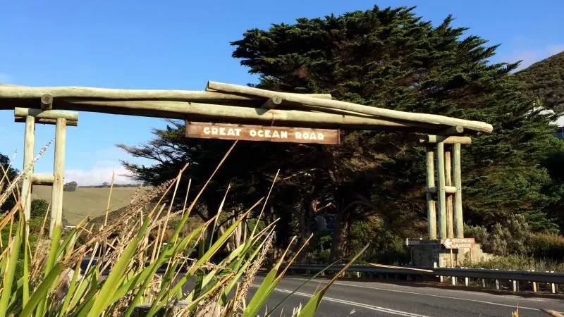 Iconic wooden archway entrance to the 1 Day Great Ocean Road 12 Apostles Tour by Go West Tours, surrounded by lush greenery and blue sky.