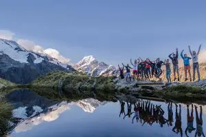 Image of a group of travellers visiting Mount Cook in New Zealand, showing the reflective waters and snowy mountains 