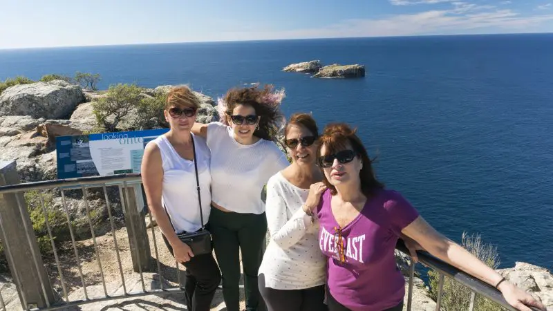 Four women admire breathtaking Wineglass Bay sea views from a scenic cliff railing on a sunny Richmond full-day tour.