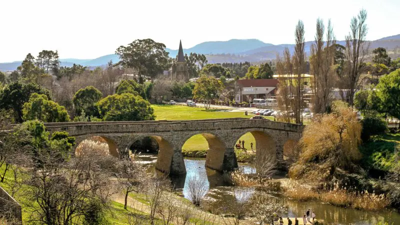 Richmond’s iconic historic stone bridge, surrounded by lush green parklands under a clear sky, featured on the Wineglass Bay Tour.