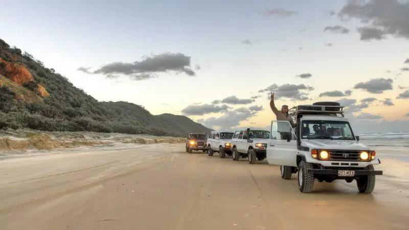 Experience five powerful 4WD vehicles exploring sandy shores on a top-rated 3 Day K'gari Fraser Island Tag Along Adventure; leader waves.