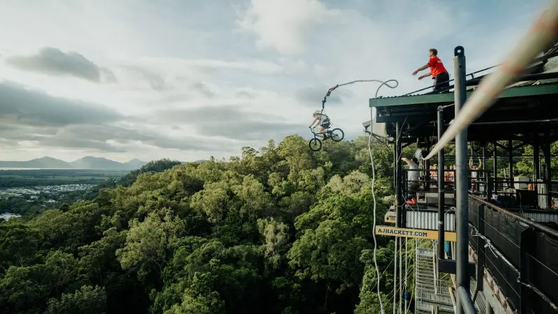 Thrill-seeker on BMX bike bungee jumping from platform at Australia’s only bungy Skypark, assisted by safety operator.