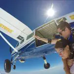 Experience the thrill of a Skydive Sydney tandem jump as two people leap from an aeroplane, surrounded by sunlit skies and scenic clouds.