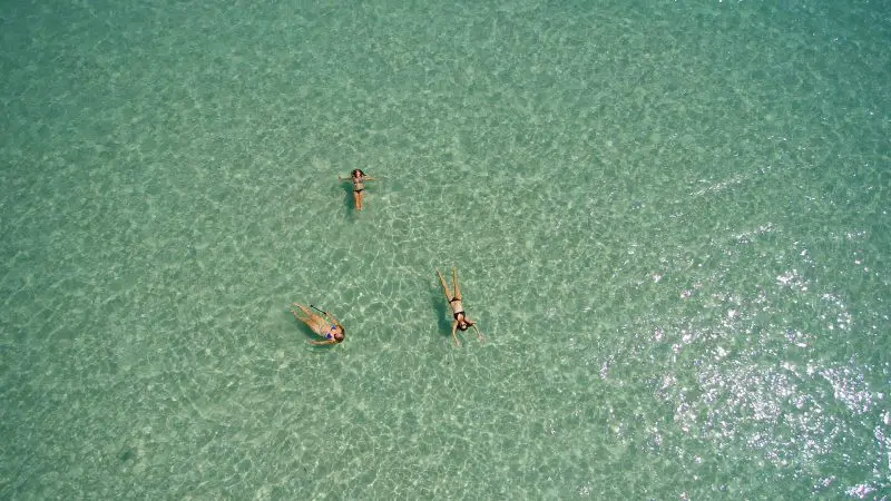 Three people relax floating on crystal-clear turquoise waters during a Remote 1 Day K'gari Fraser Island tour experience in Australia.