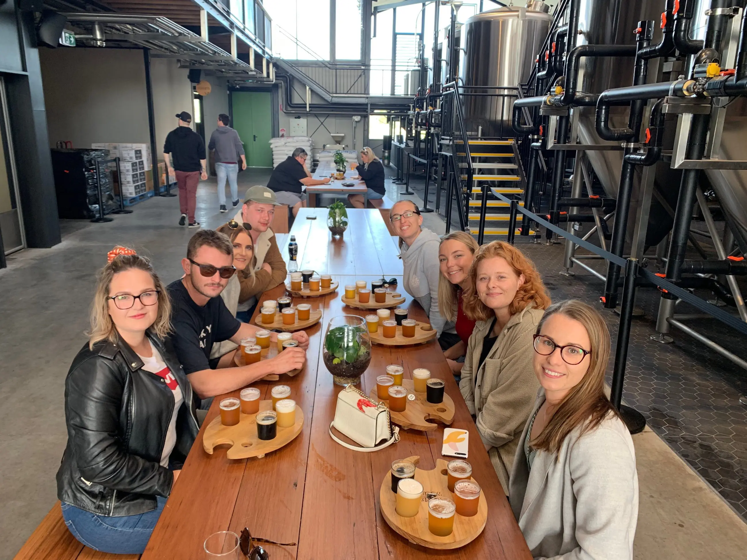Smiling group tasting craft beer flights at a vibrant brewery during an Arvo Session Behind The Barrel Half Day Tour, posing for photo.