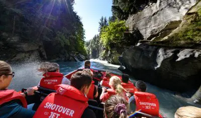 Adventurers in red life jackets experience a high-speed Shotover Jet ride through Queenstown’s dramatic, sunlit rocky gorge.