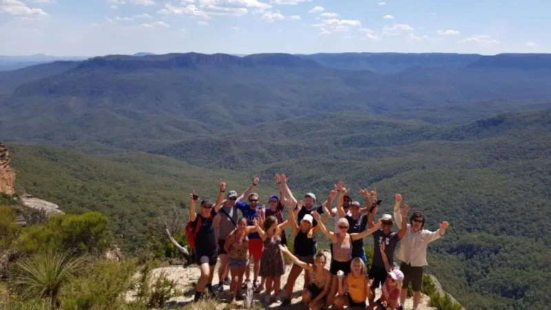 Smiling group celebrates on a rocky Blue Mountains lookout after a scenic waterfall walk and social lunch during guided day tour.