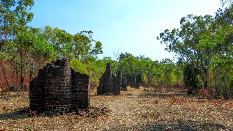 Ancient stone building ruins nestled among lush trees on a Kakadu Arnhem Land Tour, with clear blue skies overhead.