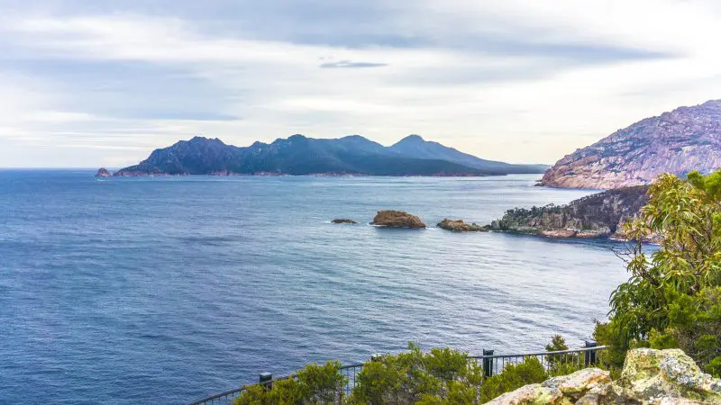 Stunning rocky coastline, vibrant blue ocean, and distant mountains seen on Wineglass Bay Full Day Tour via Richmond in Tasmania.