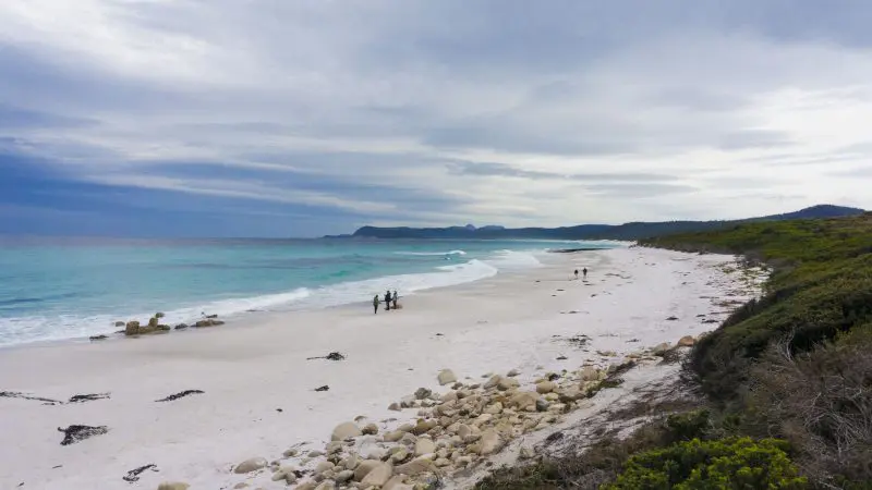 Explore Wineglass Bay’s expansive sandy beach and stunning turquoise waves on the Full Day Tour via Richmond, beneath a dramatic sky.
