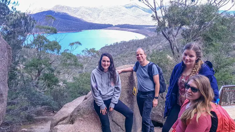 Four travellers pose on sunlit rocks overlooking Wineglass Bay with Richmond tour views, capturing Tasmania’s scenic beauty on a clear day.
