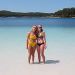 Two women in swimming costumes smile in crystal-clear water during a 3 Day K'gari Adventure with dormitory accommodation at Rainbow Beach.