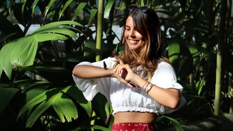 Smiling woman in sunlight at Private Exclusive Grand Kuranda, surrounded by lush greenery, butterfly gently perched on her hand.
