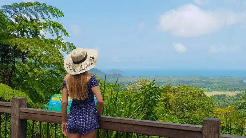 Woman in sunhat and dress gazes over Cape Tribulation Daintree Wilderness Tour’s lush rainforest with panoramic sea views.