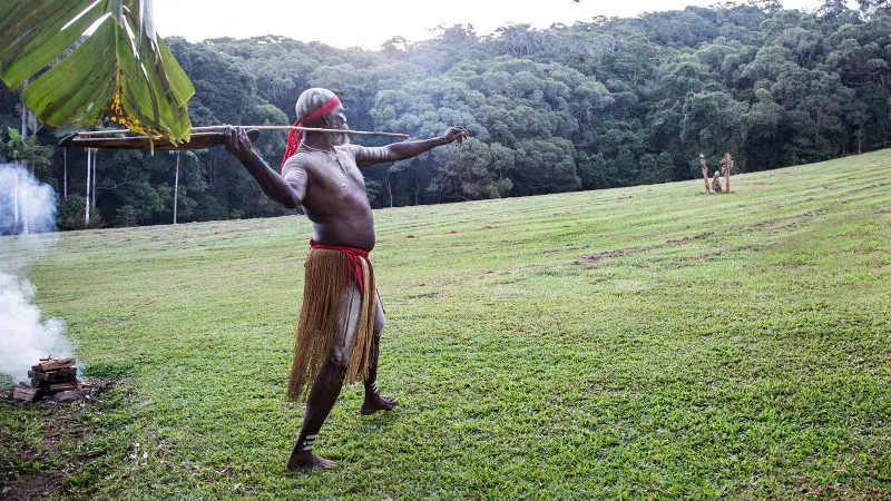 Participant in authentic cultural attire poses with a spear on lush grass at a Private Exclusive Grand Kuranda tour experience.