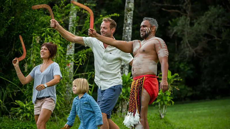 Group of four, including a child and man in Indigenous attire, smiling and holding boomerangs at Rainforestation Ckb Tour.
