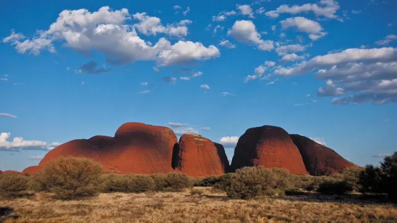 Stunning red rock formations tower over golden dry grass during the 3 Day Uluru Rock The Centre Tour from Alice Springs, Australia.