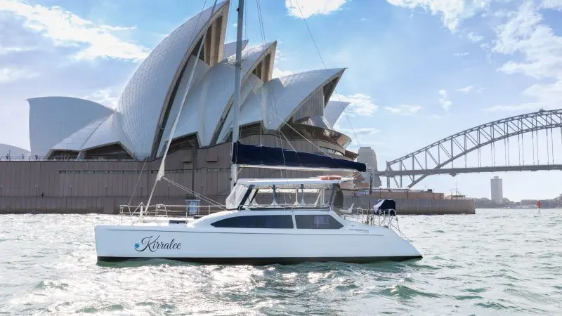 Experience a stunning Aussie Bites cruise as a white catamaran glides by Sydney Opera House and Harbour Bridge in iconic Sydney Harbour.
