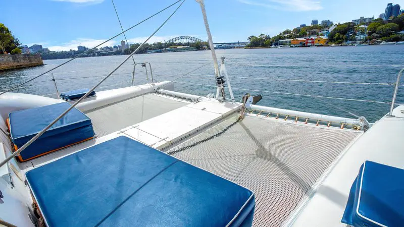 Scenic view from a luxury catamaran deck with blue cushions, overlooking Sydney Harbour icons and the city skyline in the distance.