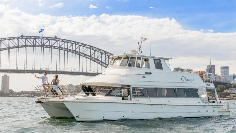 Luxury white yacht gliding on Sydney Harbour, two guests at the bow enjoying canapés during an exclusive Vivid Lights cruise experience.