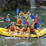Thrill-seekers white water raft Barron River with Raging Thunder, smiling by stunning waterfall on a half-day adventure tour.