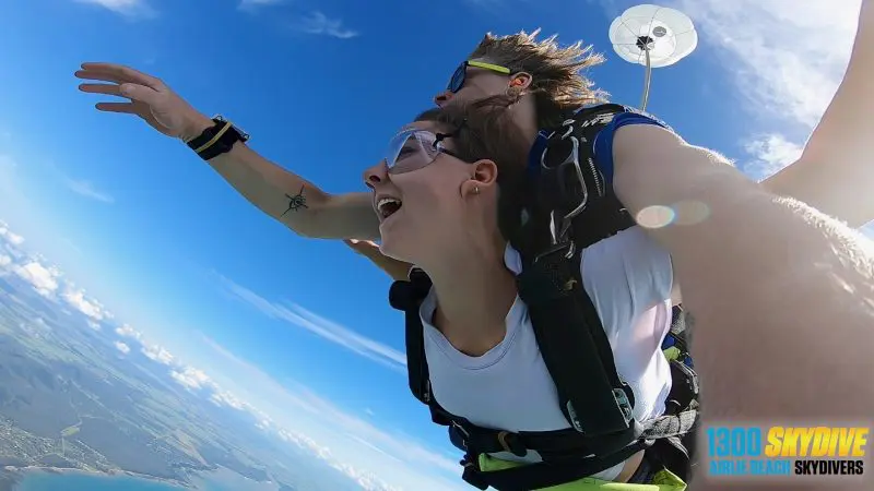Tandem skydivers with Airlie Beach Skydivers free-fall above clouds and stunning landscape, experiencing ultimate adventure.