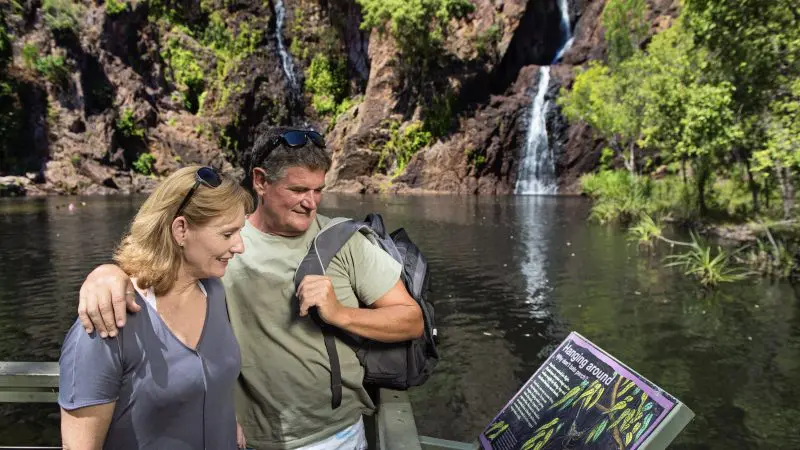 A couple studies an informative sign beside a scenic lake during a 3 Day Kakadu Litchfield National Park 4WD Safari Adventure Tour.