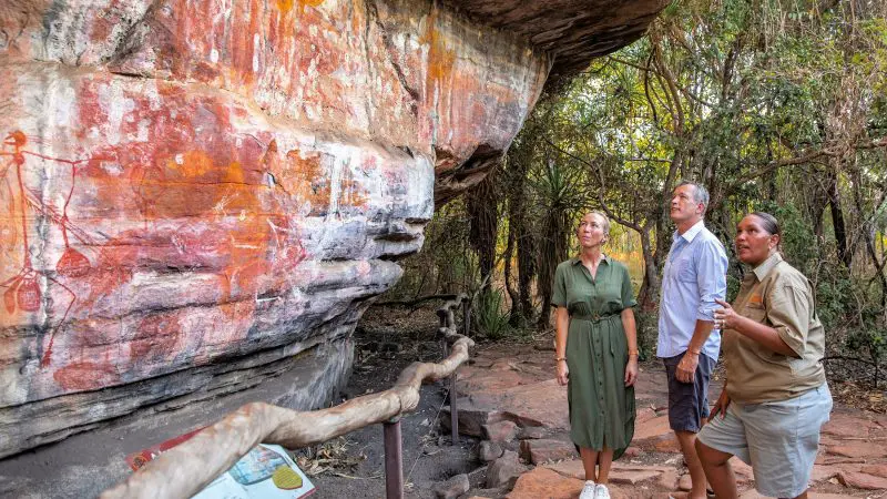 Three travellers on the 4-Day Kakadu Katherine Gorge tour from Darwin admire ancient Aboriginal rock art displayed on a rugged cliff.