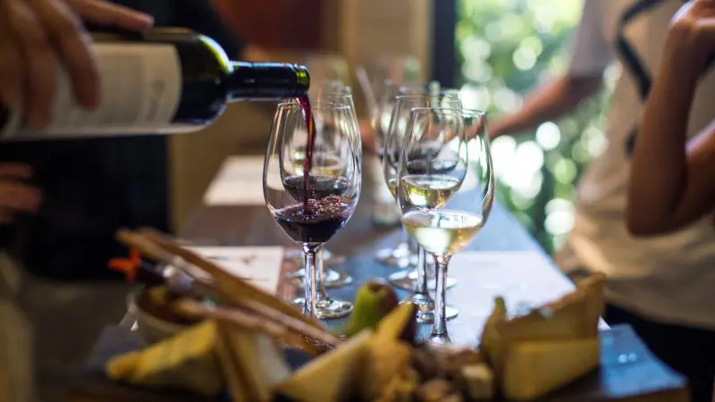 A person pours rich red wine next to elegant white wine glasses and gourmet cheese on a premium 1 Day Hunter Valley Wine Tour.